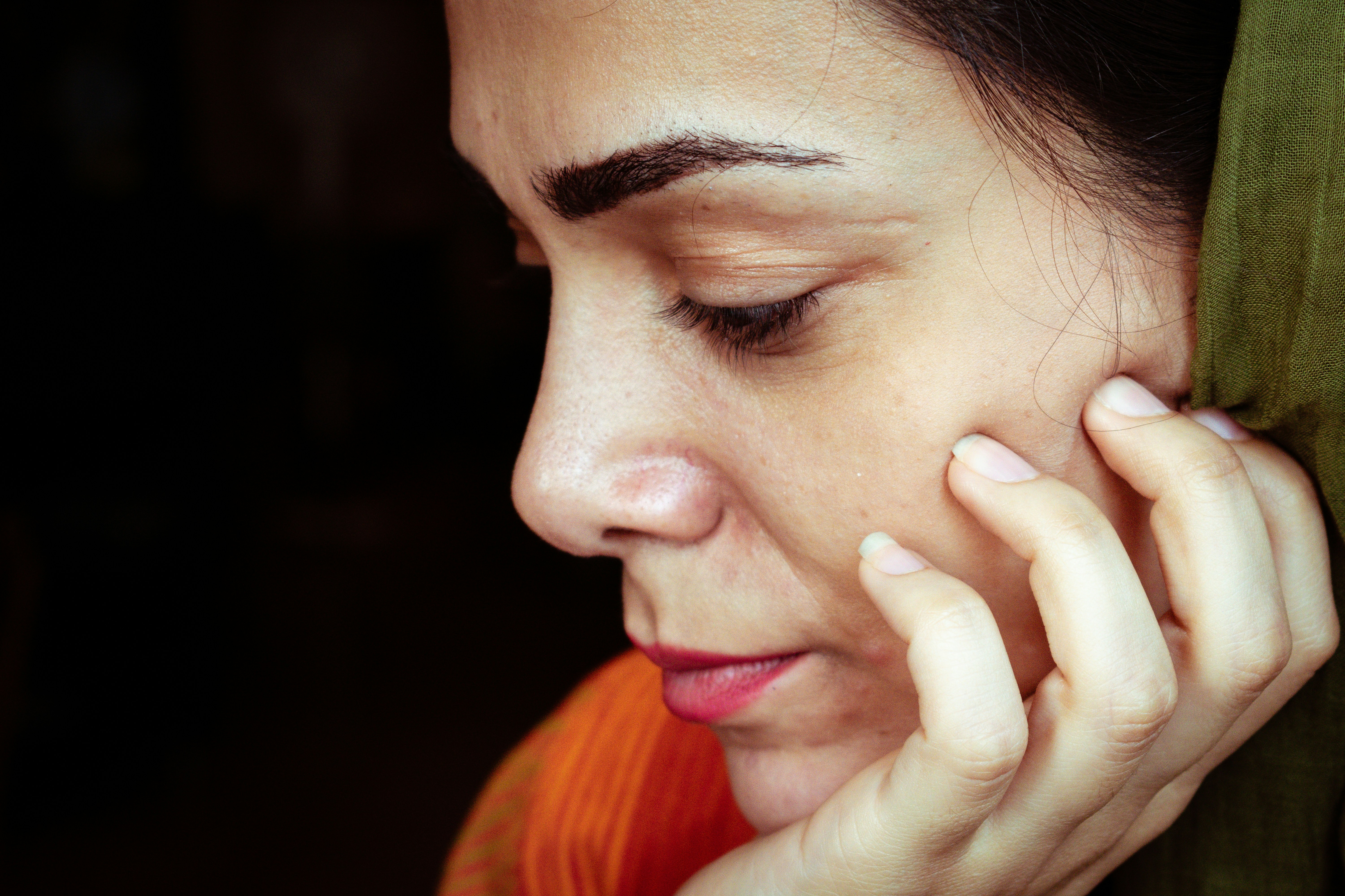 A woman resting her fingertips on her cheek, looking down in soft light