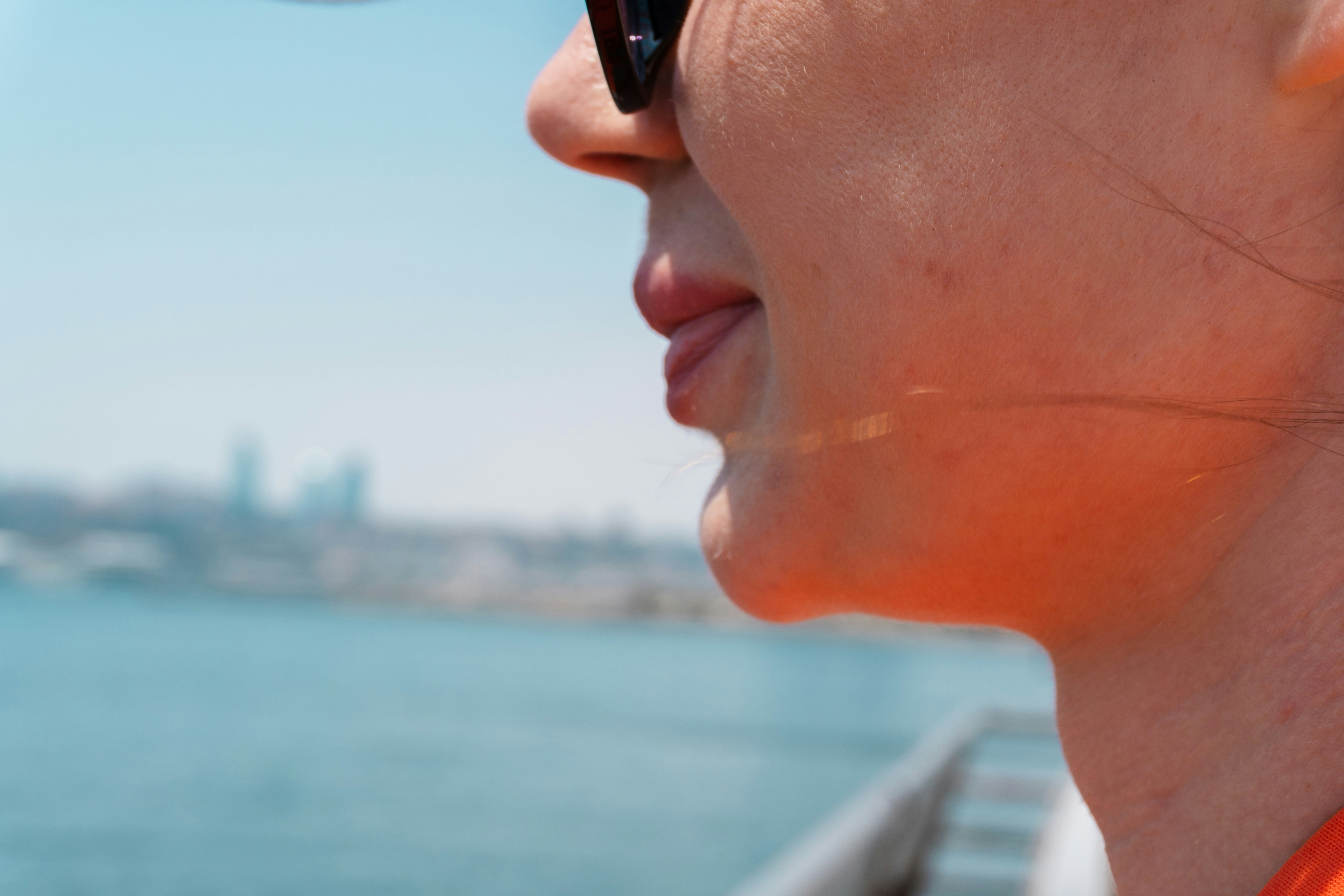 A woman by the water in bright sun, her cheek and jaw catching the light
