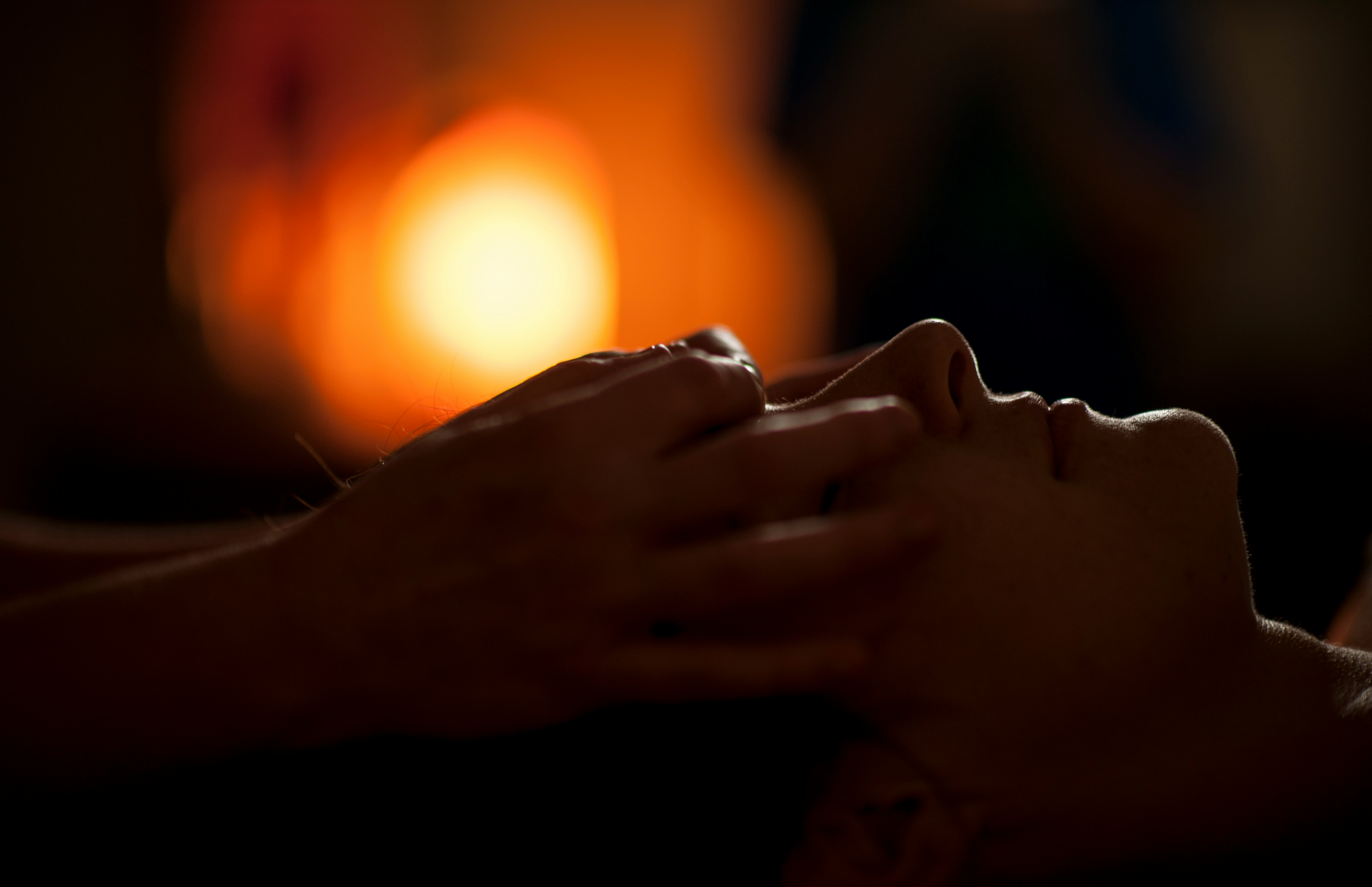 A provider’s hands resting on a client’s face in a dim, warm treatment room