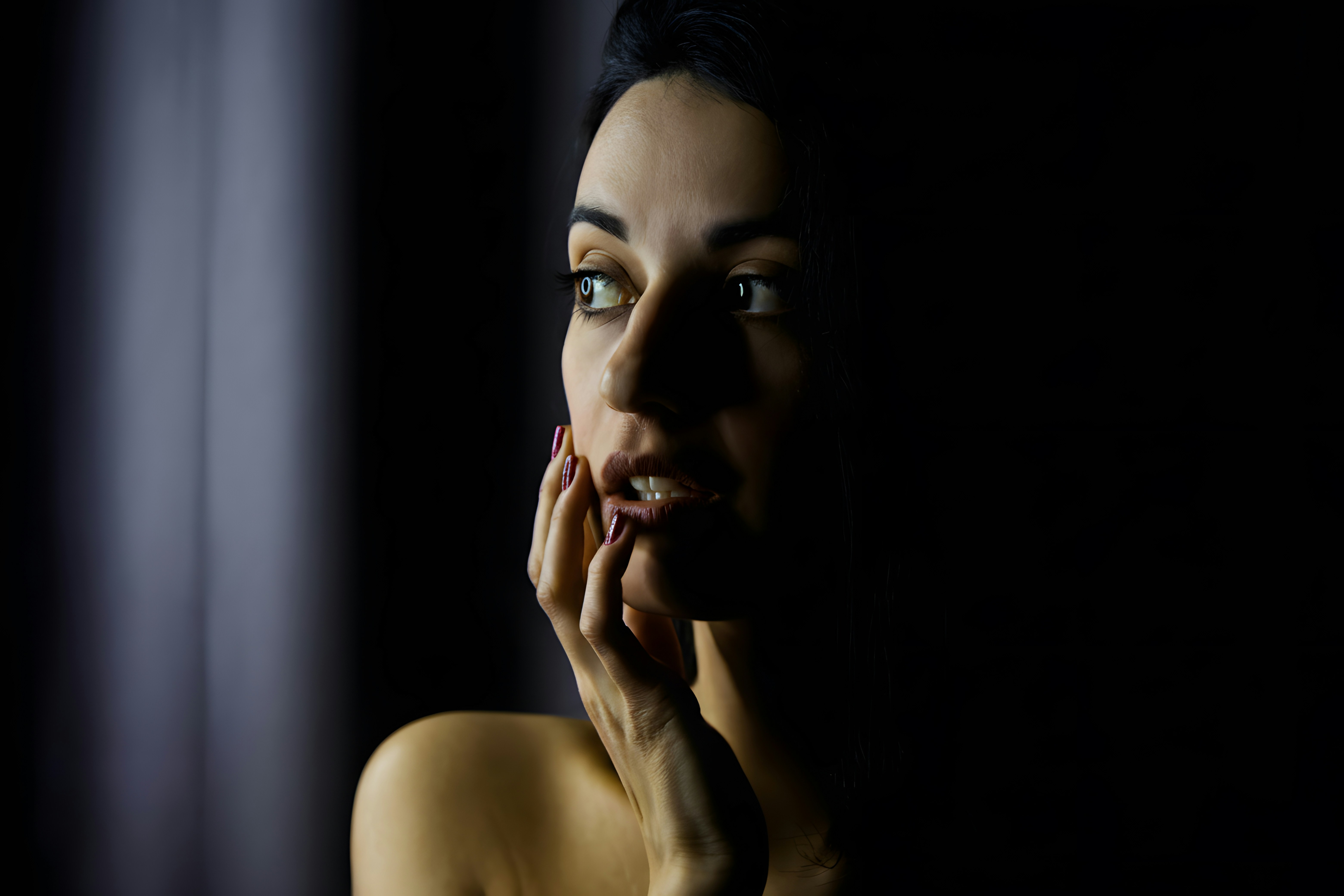 A woman touching her cheek in low light, looking to one side