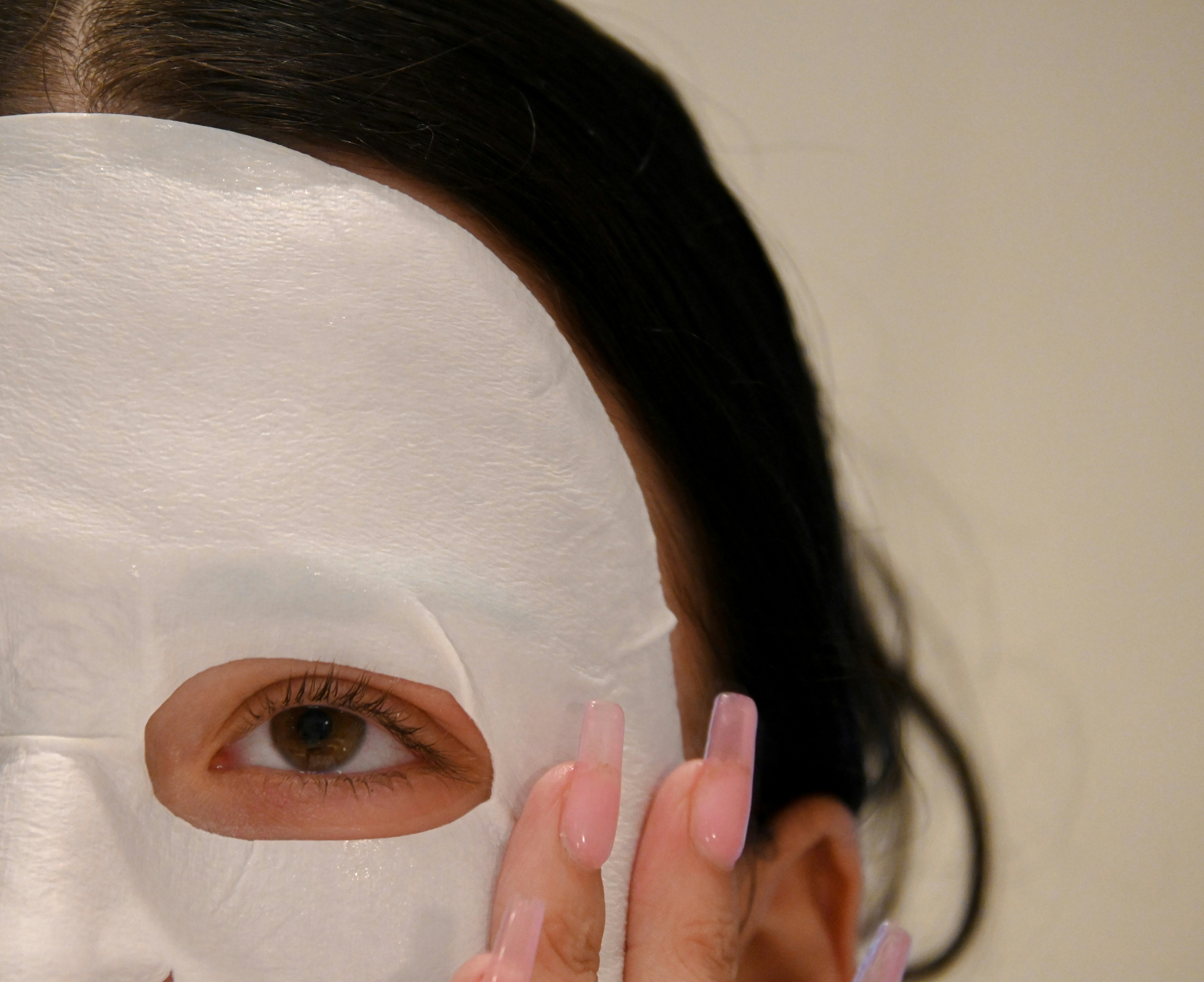 A woman holding a white sheet mask to her face