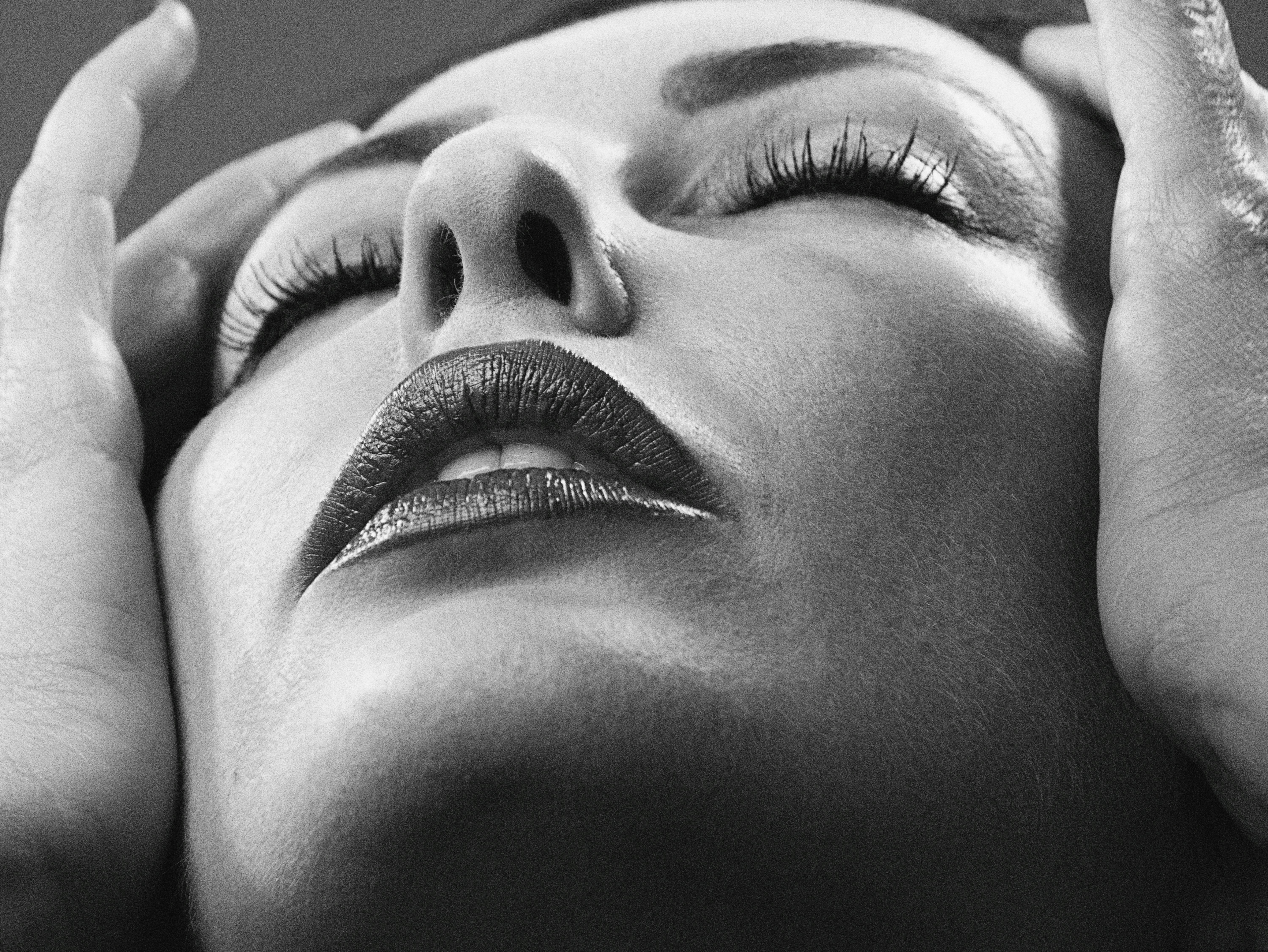Black-and-white close-up of a woman with her eyes closed and hands at her temples